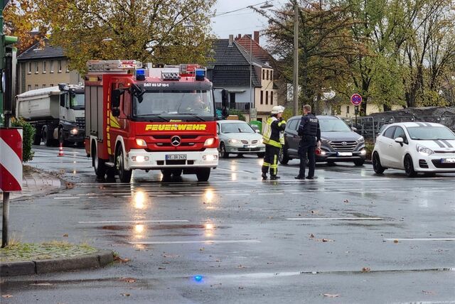 Ein Feuerwehrfahrzeug blockiert eine Straße, daneben ein Feuerwehrmann und ein Polizist.