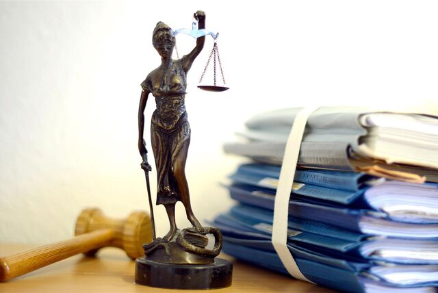 Die modellhafte Nachbildung der Justitia steht in einem Raum eines Richters neben einem Holzhammer und einem Aktenstapel.
