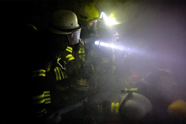 Zwei Feuerwehrleute mit einer Taschenlampe in einem dunkle, vernebelten Haus bei einer Übung.