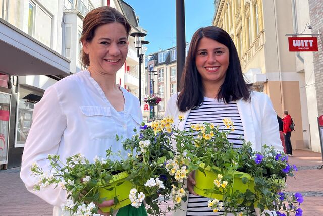 Anika Levin und Yasemin Breilmann von der Frauen Union stehen in der Castroper Innenstadt und haben jeweils eine Blumenampel in der Hand.