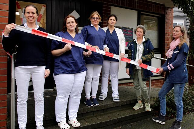 Ärztinnen und  Apothekerinen halten rot-weißes Flatterband hoch.