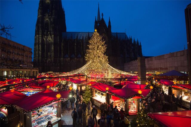 Stände mit roten Dächern und eine beleuchtete Fichte stehen auf dem Domplatz vor dem Dom.