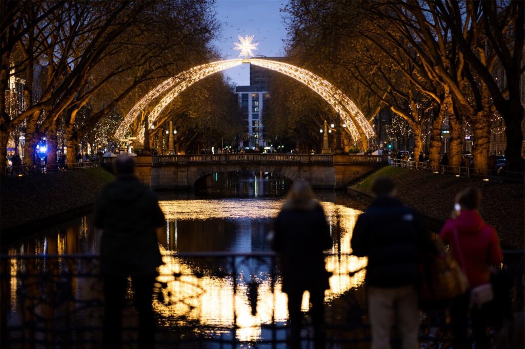 Passanten betrachten während des Weihnachtsmarktes in Düsseldorf die Lichter-Deko an der Königsallee. Passanten betrachten während des Weihnachtsmarktes in Düsseldorf die Lichter-Deko an der Königsallee.