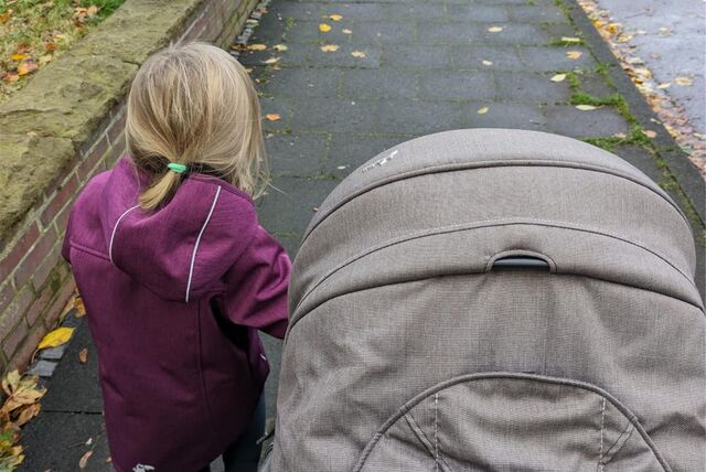 Ein Kind geht neben einem Kinderwagen auf dem Bürgersteig.