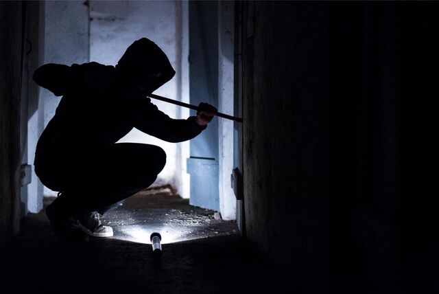 Einbrecher im Hoodie mit einer Brechstange an einem Fenster.