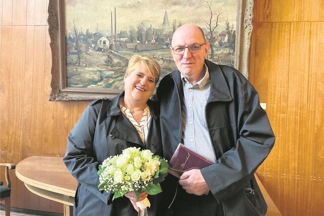 Ein Paar im Waltrop Ratssaal mit weißen Rosen und Stammbuch in der Hand.