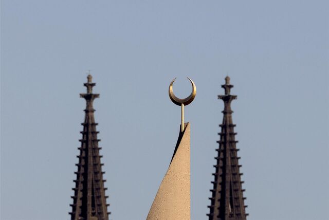 Ein Halbmond auf einer Moschee ist zwischen den Türmen des Kölner Doms zu sehen.