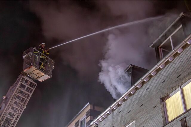 Ein Feuerwehrmann steht auf der Drehleiter. Er löscht ein Feuer in einem Wohnhaus.