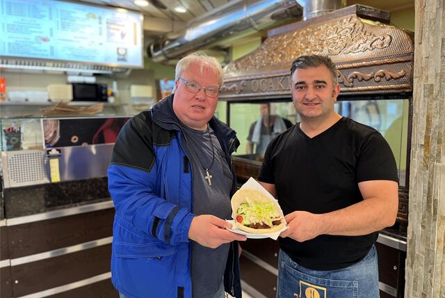 Thomas Frauendienst (l.) und Selam Tasdemir stehen vor einem Grill und halten einen Teller mit einer Dönertasche in den Händen.