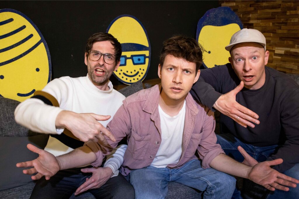 Die drei Sänger von der Band Deine Freunde schauen sitzen auf einer Couch und schauen in die Kamera