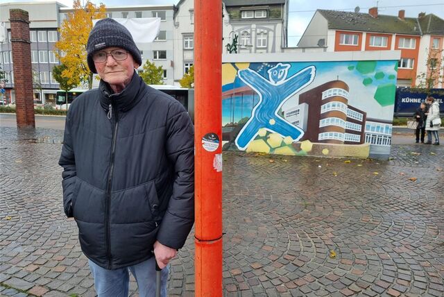Ein Mann lehnt an einer Laterne auf einem Marktplatz.
