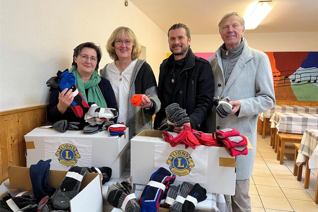 Vier Menschen, zwei von der Caritas und zwei vom Lions Club Philipp von Viermundt, stehen hinter vier Kartons, die gefüllt mit Socken sind.