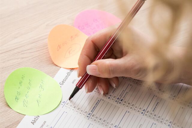 Eine Person schreibt mit einem roten Stift Termine in den Kalender