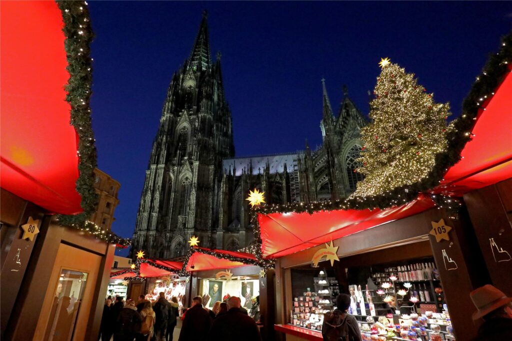 Besucher gehen über den Weihnachtsmarkt vor dem Dom