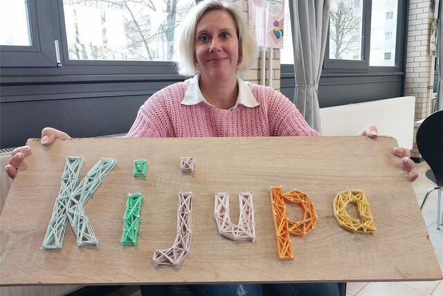 Eine Frau hält ein Holzschild „KiJuPa“ in der Hand