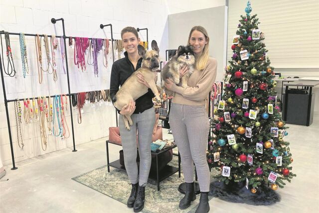 Zwei junge Frauen mit Hunden auf dem Arm stehen in einer Ausstellungshalle des Unternehmens Puppyrope in Waltrop neben einem geschmückten Weihnachtsbaum.