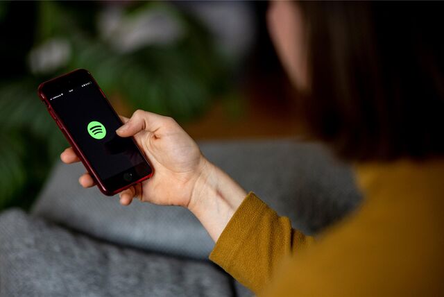 Eine Frau hält ein Smartphone in der Hand, auf dem das Spotify-Logo zu sehen ist.