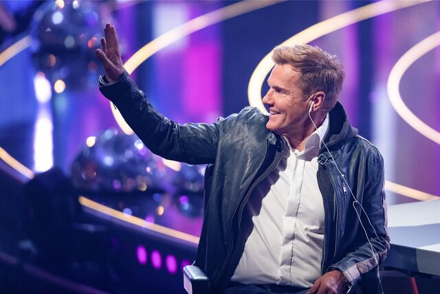 Dieter Bohlen sitzt am Jury-Pult und grüßt das Publikum.