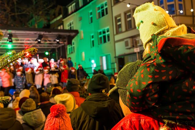 Ein Mädchen sitzt auf dem Recklinghäuser Kirchplatz auf den Schultern eines Mannes und beobachtet den Auftritt eines Kinderchores auf einer Bühne.