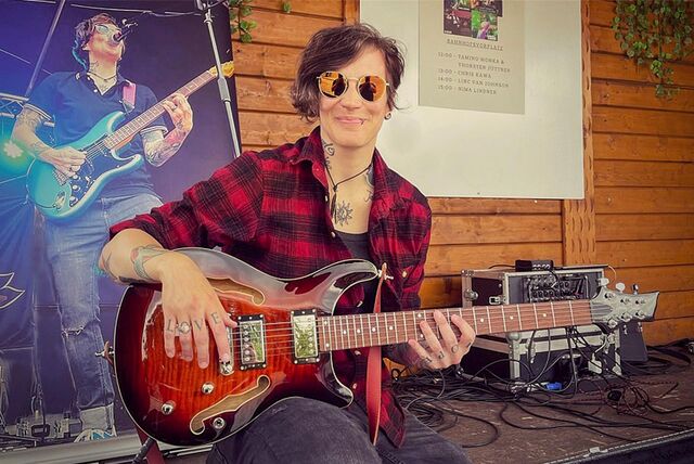 Musikerin NiMa Lindner sitzt auf einer Bühne, in den Händen hält sie eine E-Gitarre.