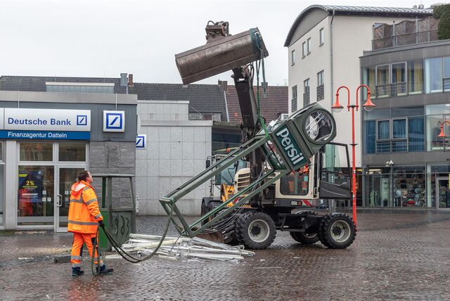 Das Gerüst einer Uhr wird von einem Bagger in die Höhe gehoben.