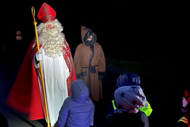 Nikolaus schaut auf zwei Kinder, die mit dem Rücken zur Kamera stehen.