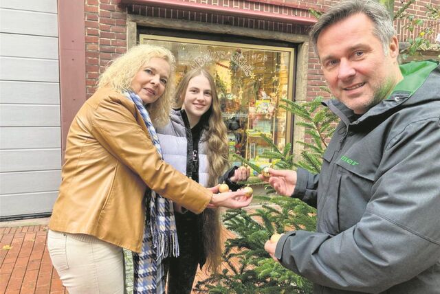 Eine Frau, ein junges Mädchen und ein Mann schmücken einen Christbaum in der Waltroper Fußgängerzone.