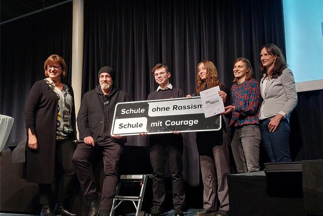 Schulleiterin Astrid Fuhrmann, Comedian Torsten Sträter, die Schüler Alex und Fabienne sowie die Vertreterinnen der Regionalkoordination Kreis Recklinghausen des Netzwerkes „Schule ohne Rassismus – Schule mit Courage“ Lotte Schelleckes und Anja Boßert stehen nebeneinander auf einer Bühne.