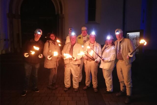 Eine Gruppe steht mit Bergkitteln, Helmen und Fackeln vor St. Michael in Hochlarmark.
