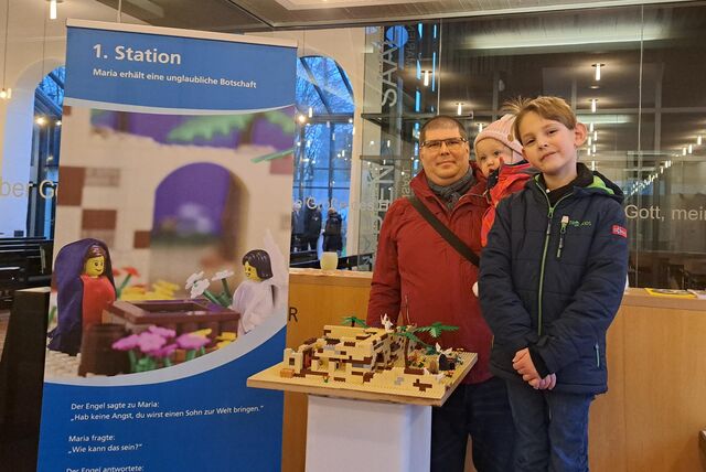 Ein Mann mit einem kleinen Kind auf dem Arm und einem Sohn vor ihm, stehen an der 1. Station: Maria erhält eine unglaubliche Botschaft.