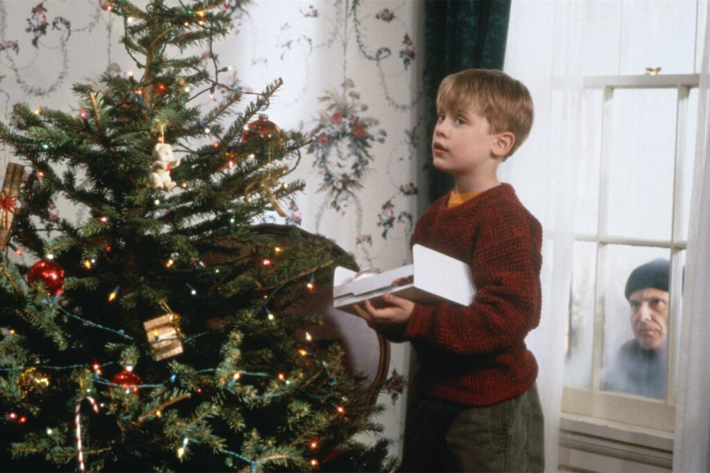 Eine Szene aus „Kevin allein zu Haus“: Kevin McCallister (Macaulay Culkin) schmückt im Haus der Familie in Chicago den Weihnachtsbaum, während Harry, einer der „feuchten Banditen“, durchs Fenster ins Haus schaut.