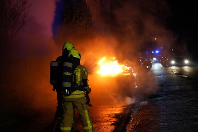 Zwei Feuerwehrleute mit Strahlrohr vor dem brennenden Motorraum eines Sportwagens.