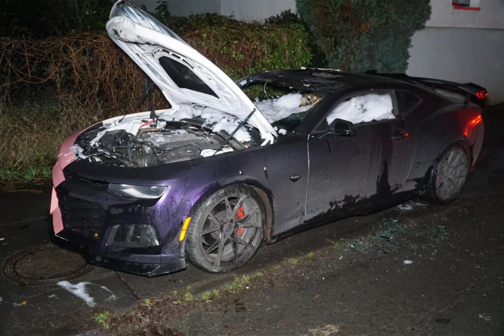 Ausgebrannter Chevrolet Camaro mit offener Motorhaube und Löschschaum im Innenraum. Ausgebrannter Chevrolet Camaro mit offener Motorhaube und Löschschaum im Innenraum.