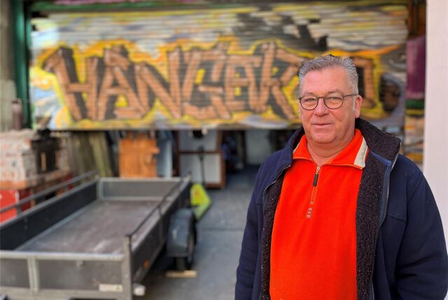Frank Holterdorf steht vor seiner Halle, in der er die Türen anfertigt. Das Rolltor ist mit einem Graffito „Hangar 70“ besprüht.