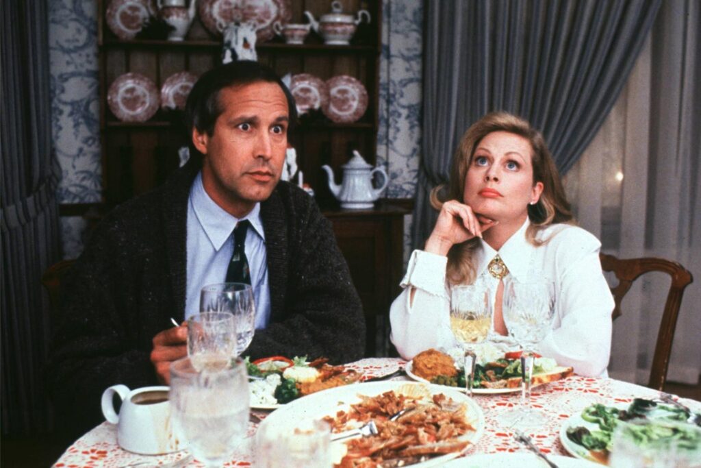 Filmszene: Clark Griswold (Chevy Chase) und Ellen Griswold (Beverly D' Angelo) sitzen zusammen am Esstisch und gucken genervt.