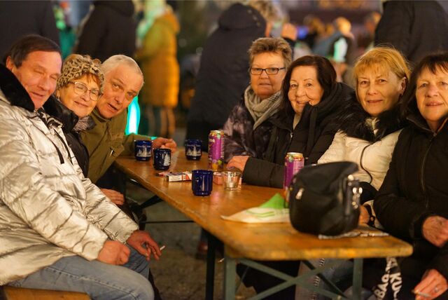 Fünf Frauen und zwei Männer sitzen nebeneinander an einer Bierzeltgarnitur und blicken überwiegend lächelnd in die Kamera. Auf dem Tisch stehen Glühweintassen, Getränkedosen und eine Handtasche.