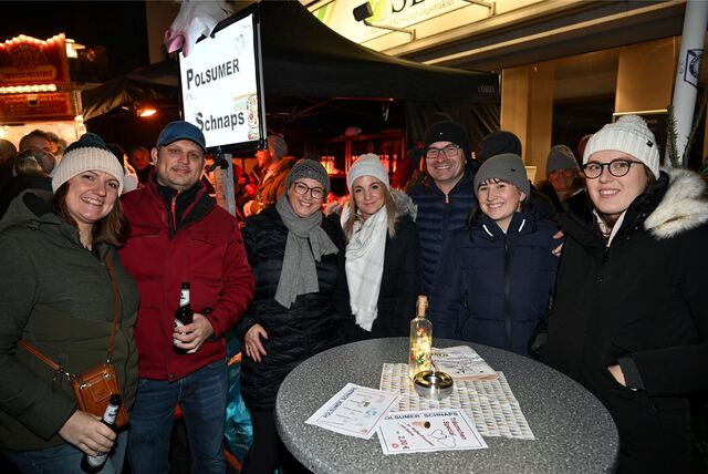 Eine Gruppe von Menschen lächelt in die Kamera. Sie stehen auf einem Weihnachtsmarkt.