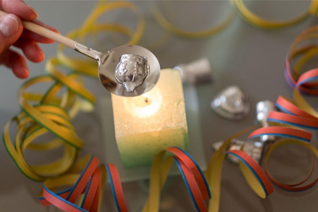 Ein Bleistück wird an Silvester über einer Kerze zum Schmelzen gebracht. Um die Kerze liegen bunte Luftschlange. Ein Bleistück wird an Silvester über einer Kerze zum Schmelzen gebracht. Um die Kerze liegen bunte Luftschlange.