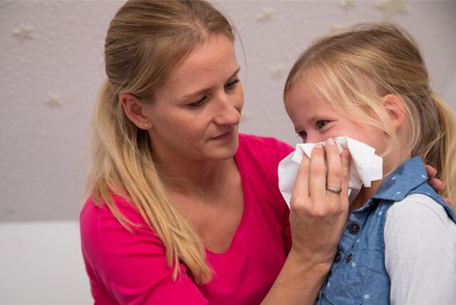 Eine Mutter putzt der Tochter die Nase.