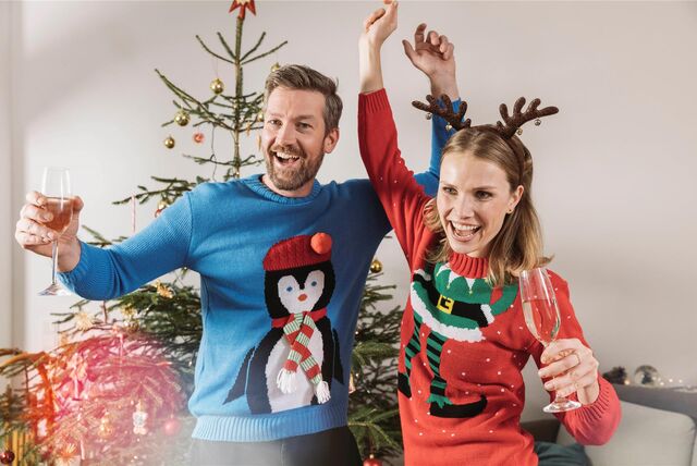 Ein Mann und eine Frau stehen vor einem Weihnachtsbaum. Sie tragen Ugly-Christmas-Sweater