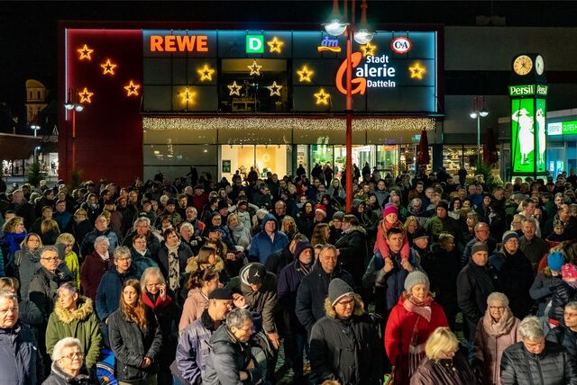 Eine Menschenmenge steht auf einem Marktplatz, im Hintergrund ein weihnachtlich geschmücktes Einkaufszentrum.