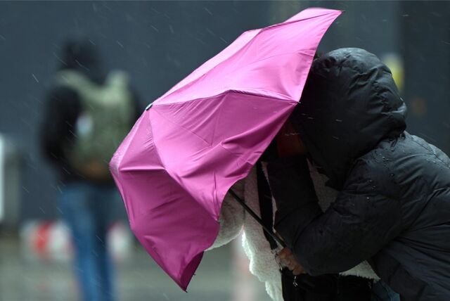 Passanten kämpfen mit dem Wind und ihrem Regenschirm.