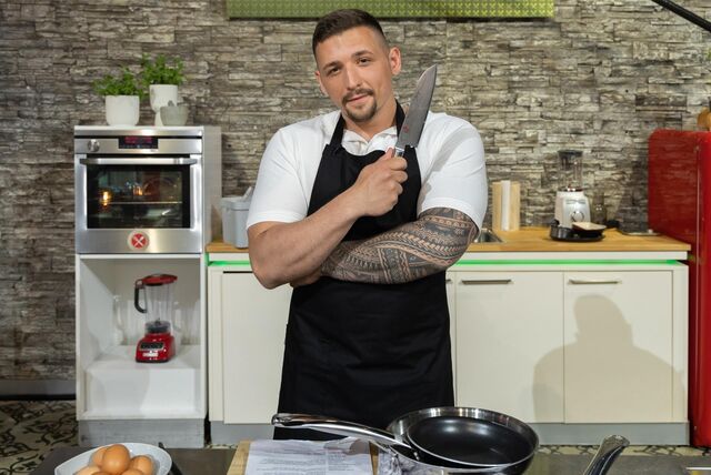 Ein junger muskulöser Mann steht in der TV-Show „Küchenschlacht“ in seiner Küche und posiert mit einem großen Messer.