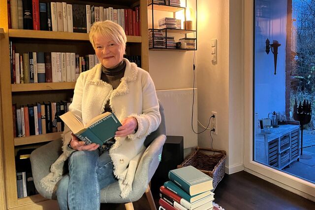 Anne Heine-Hagen sitzend mit Buch vor einem Bücherregal