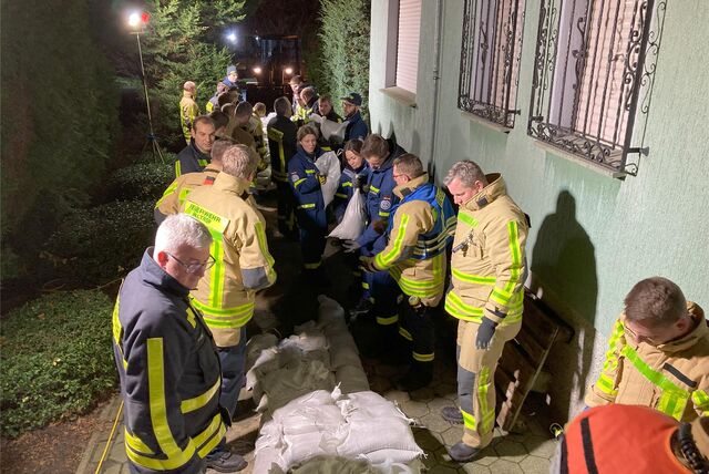 Einsatzkräfte von Feuerwehr und THW sichern ein vom Hochwasser bedrohtes Wohnhaus mit Sandsäcken.