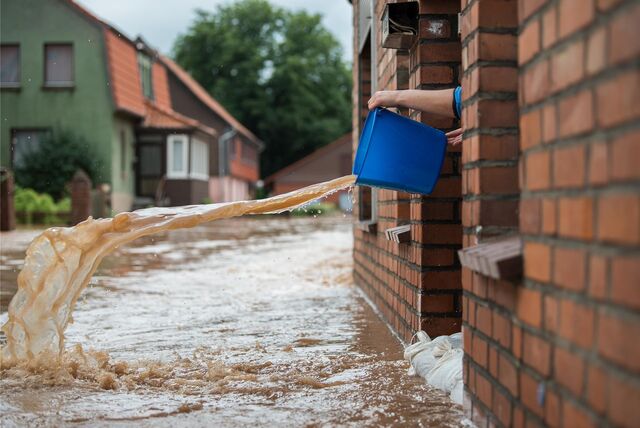 Wasser kommt aus einem Eimer, der aus einem Hauseingang geschüttet wird