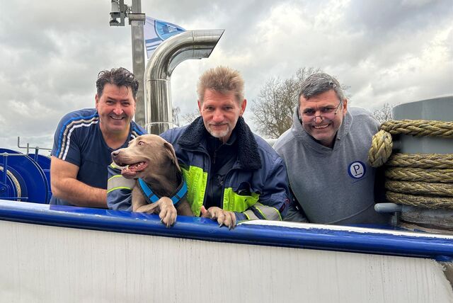 Drei Männer stehen mit einem Hund auf einem Schiff.