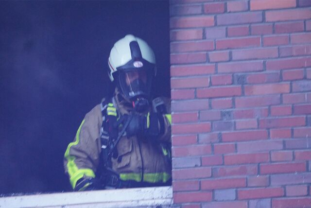 Ein Feuerwehrmann mit einer Atemschutzmaske steht in einer Fensteröffnung.