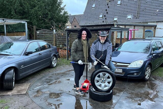 André und Katrina Schwanitz mit zwei platten Reifen zwischen Autos.