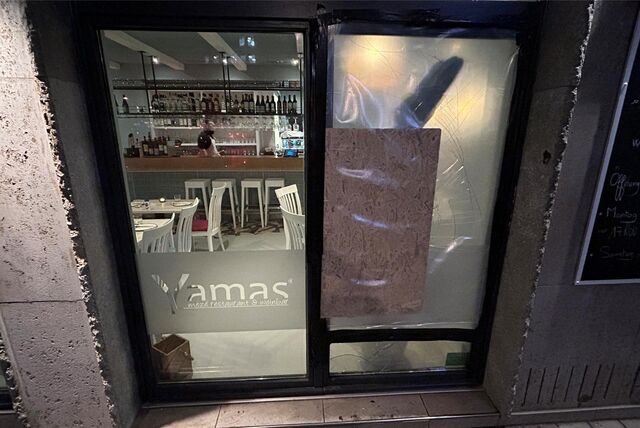 Das Restaurant Yamas von außen. Eine Glasscheibe wurde eingeworfen und mit einer Holzplatte und dicker Plastikfolie wieder zugeklebt. Hinter der Folie sieht man noch Risse im Glas.